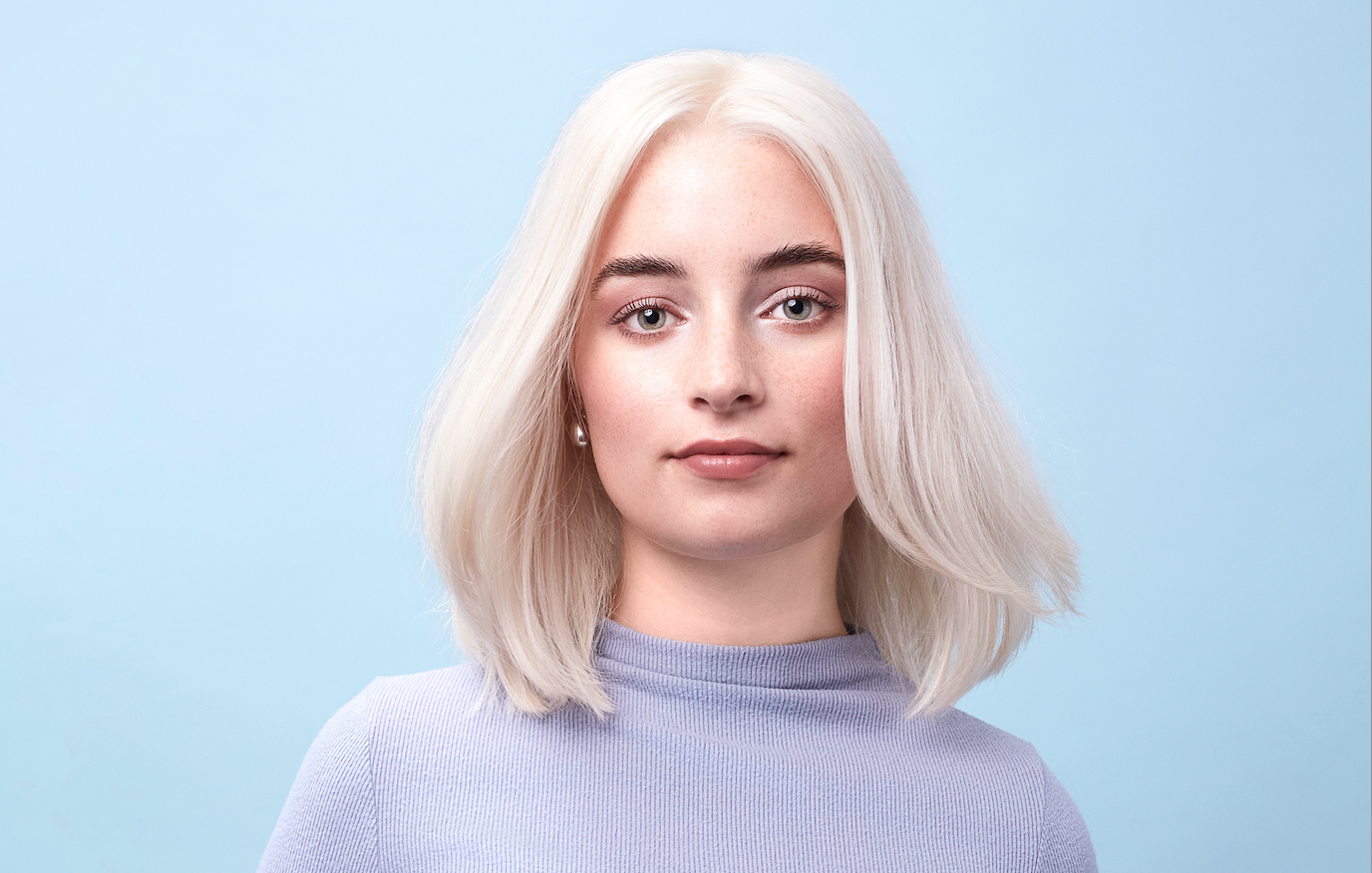 Model mit einem hellblonden Bob, heller Haut und hellen Augen vor einem hellblauem Hintergrund