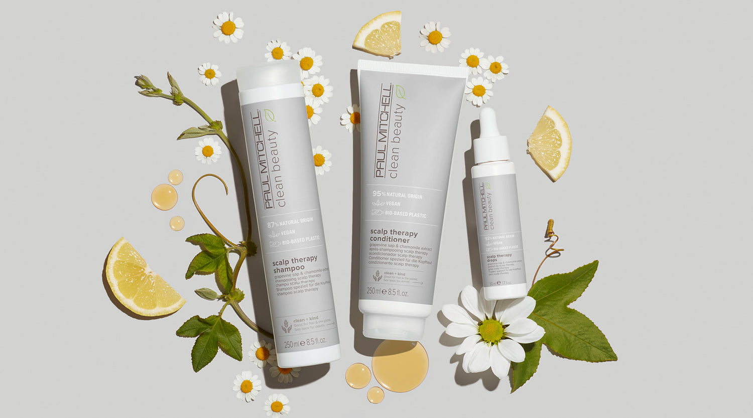 Pflegeprodukte auf grauem Hintergrund mit Weinrebenblättern, Kamille & Zitrone – beruhigt empfindliche Kopfhaut.