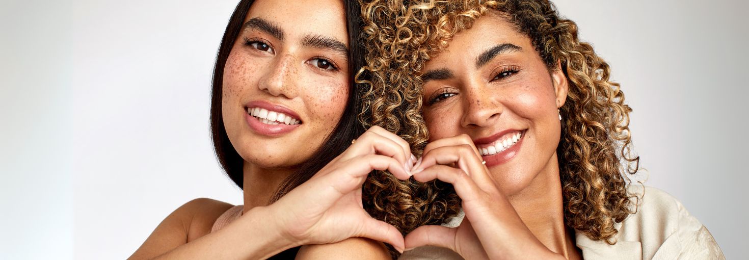 Zwei Freundinnen, die mit ihren Händen ein Herz zeigen und lächeln