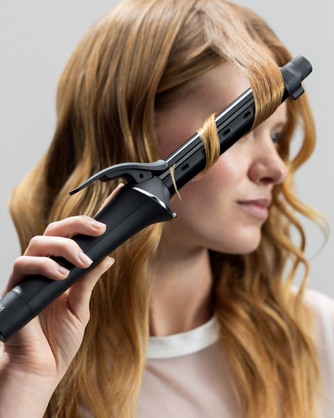 Frau mit welligem Haar, die sich gerade mit einem Stylingtool Locken ins Haar frisiert.